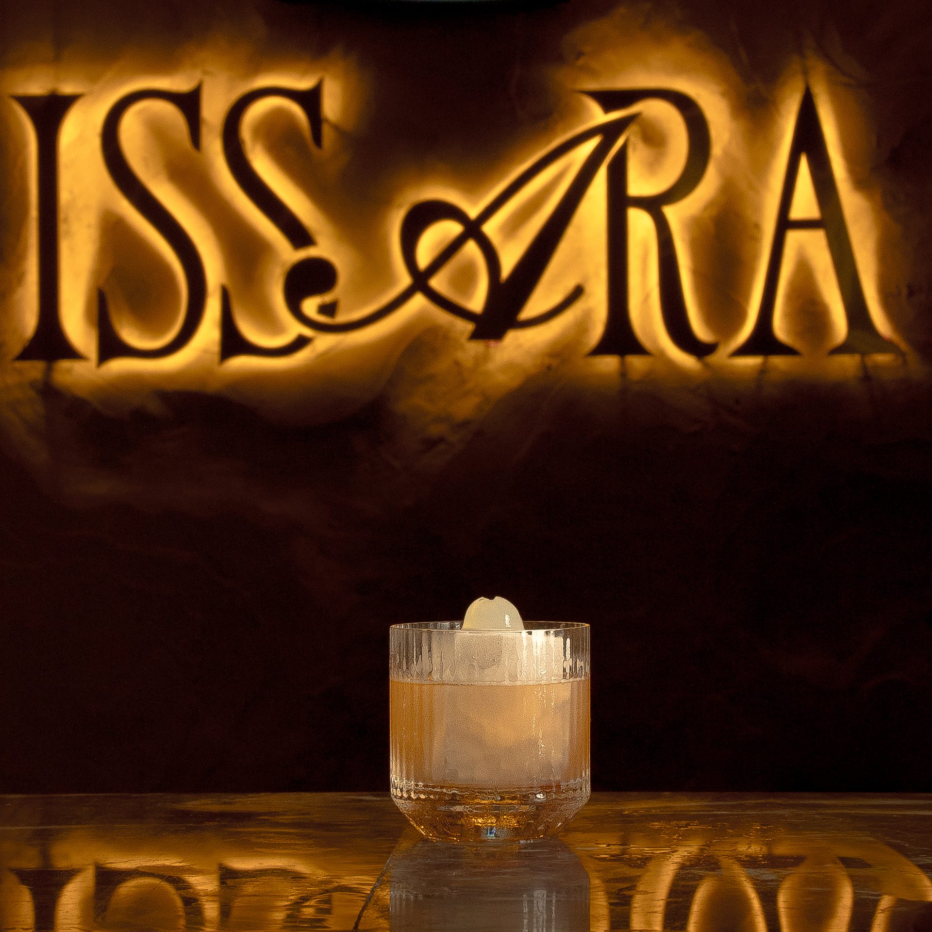 Craft cocktail on marble bar counter in front of illuminated Issara sign